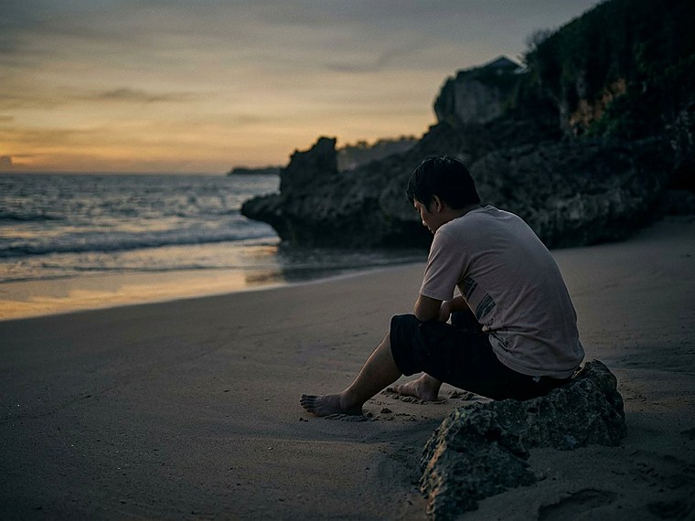 A man sitting alone on a beach at sunset